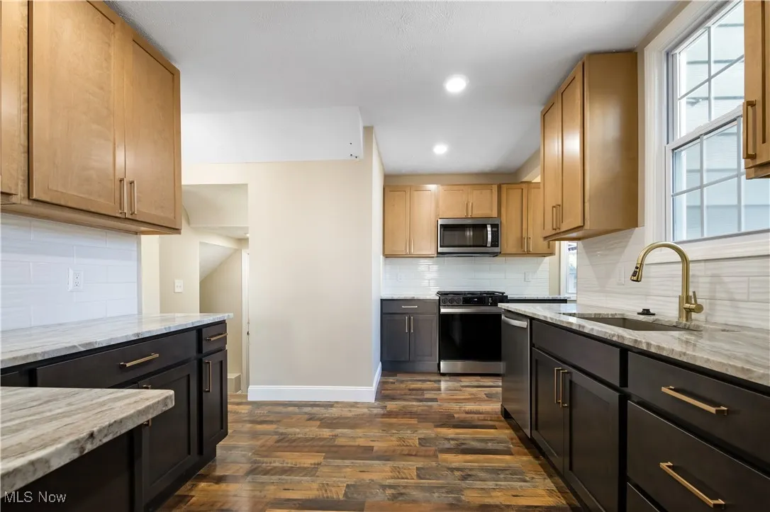 Kitchen with backsplash, stainless steel appliances, light stone countertops, dark wood finished floors, and recessed lighting