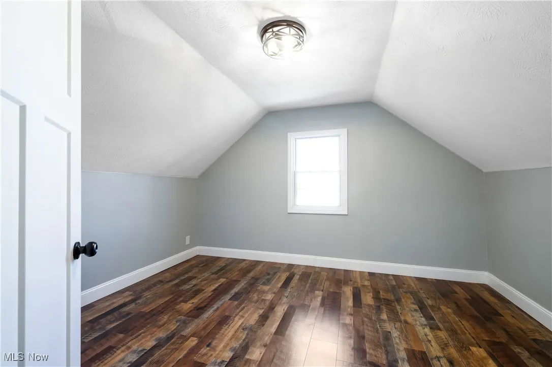 Additional living space featuring lofted ceiling, dark wood-type flooring, and a textured ceiling