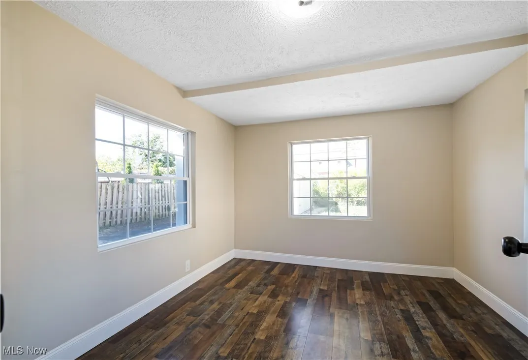 Unfurnished room with a textured ceiling, dark wood-style floors, and plenty of natural light