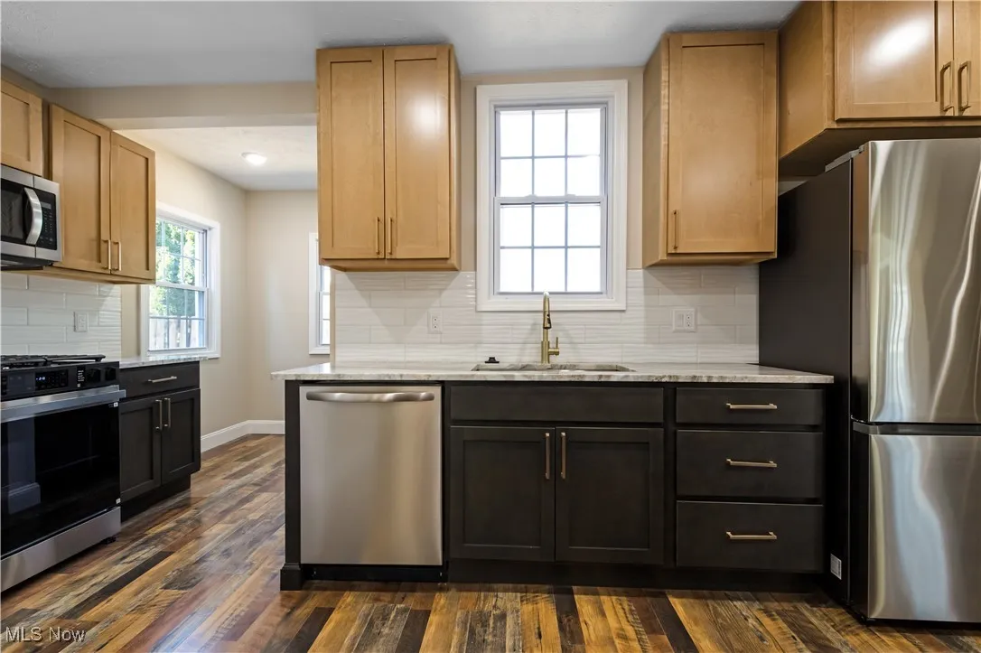 Kitchen with appliances with stainless steel finishes, light stone countertops, tasteful backsplash, and dark wood-type flooring