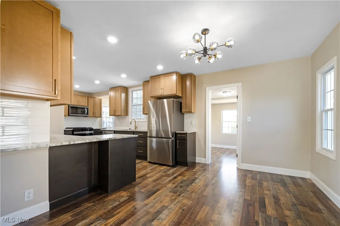 Kitchen with stainless steel appliances, a peninsula, tasteful backsplash, dark wood finished floors, and a chandelier