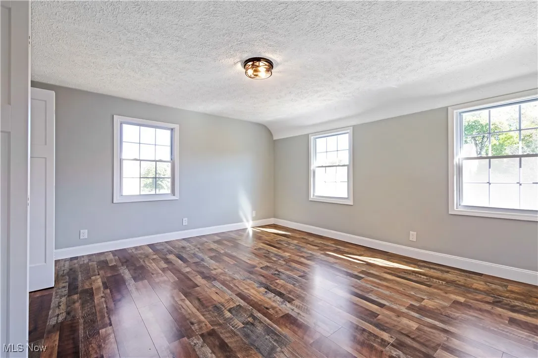 Spare room with dark wood finished floors, a textured ceiling, and lofted ceiling