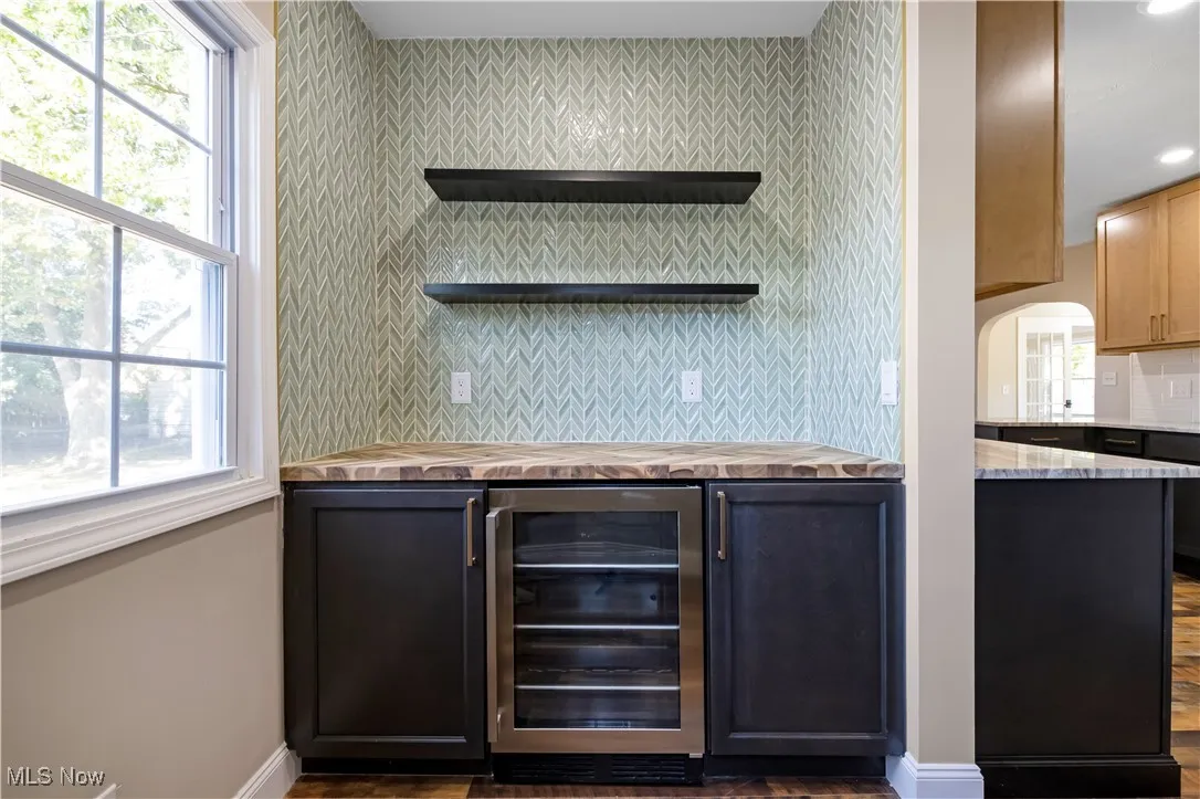 Bar area featuring decorative backsplash, wine cooler, dark cabinets, open shelves, and plenty of natural light