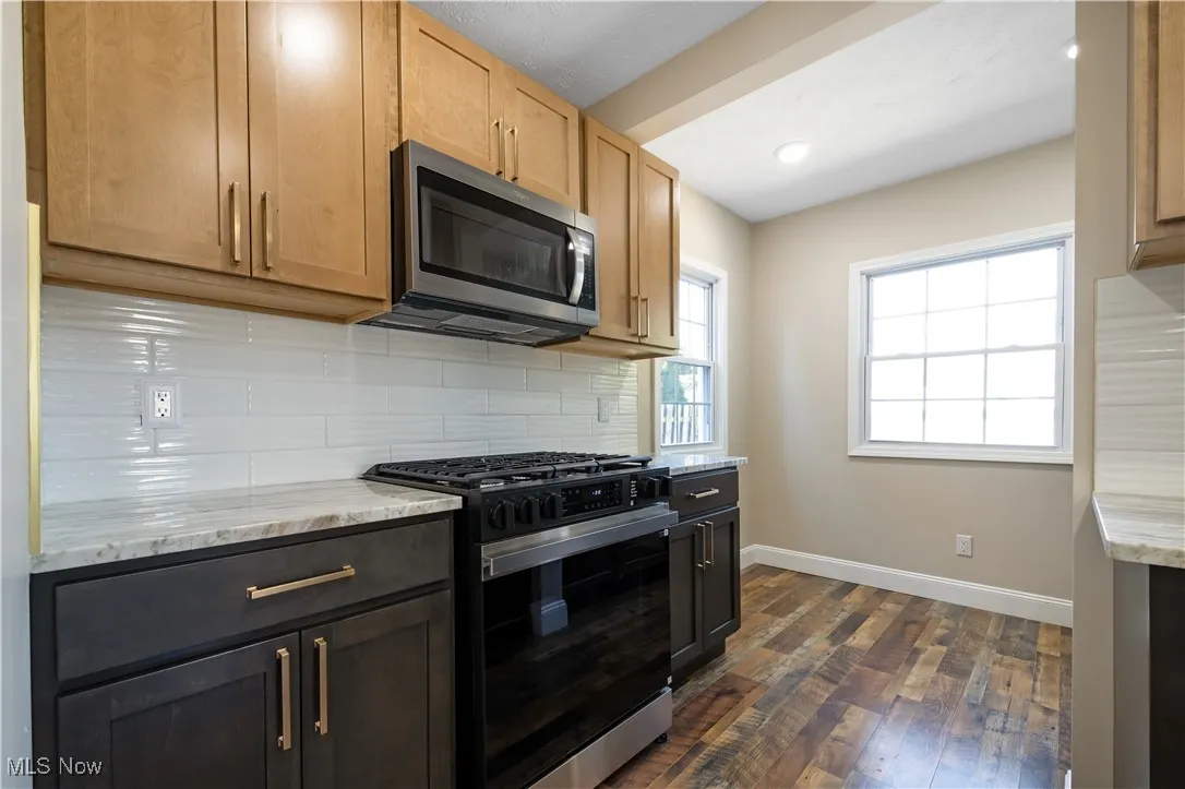 Kitchen with gas stove, tasteful backsplash, stainless steel microwave, light stone counters, and recessed lighting