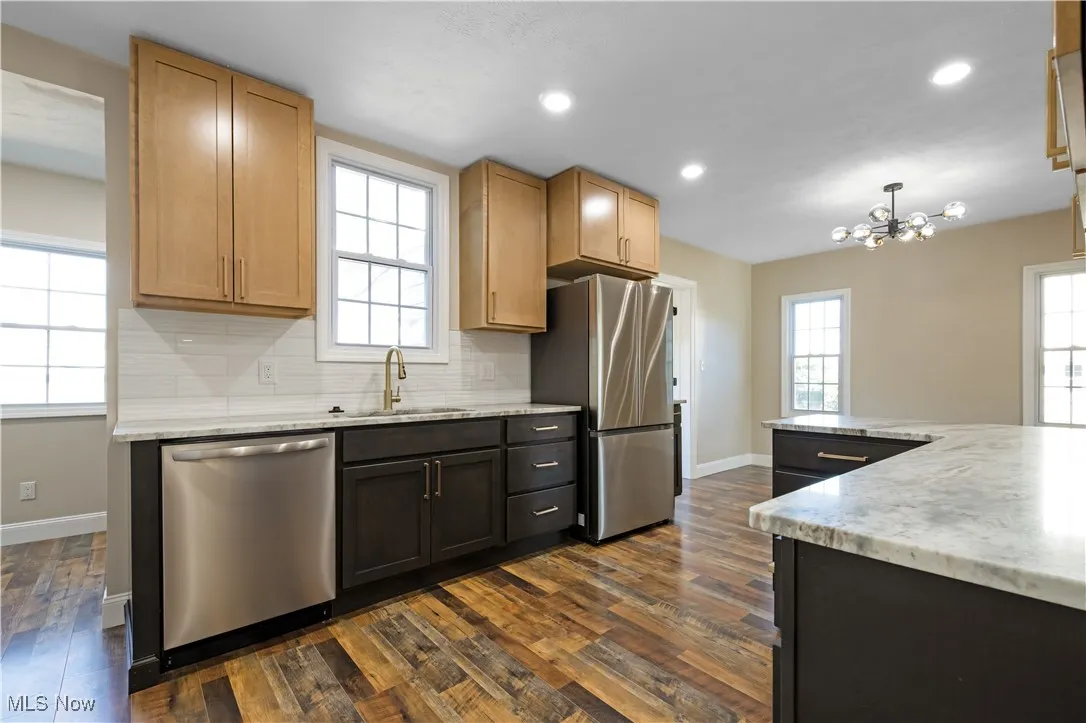 Kitchen featuring backsplash, appliances with stainless steel finishes, light stone countertops, hanging light fixtures, and recessed lighting