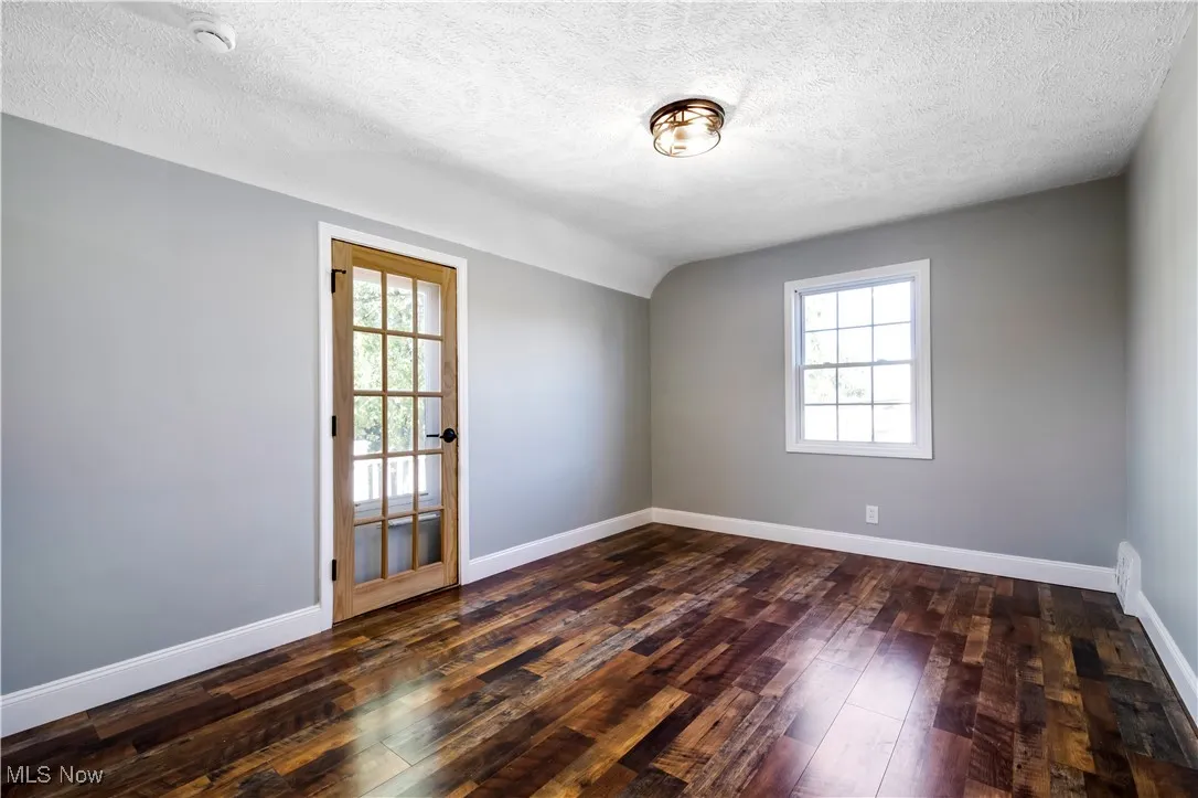 Empty room with plenty of natural light, dark wood-style flooring, a textured ceiling, and vaulted ceiling