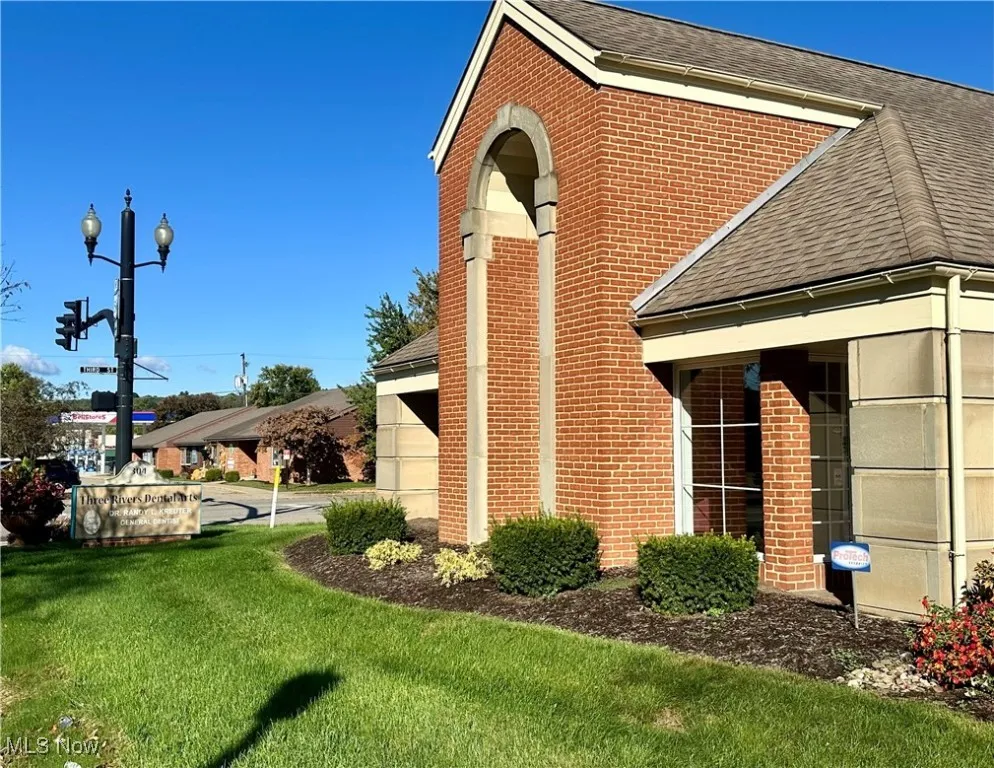 View of side of property featuring roof with shingles, a lawn, and brick siding