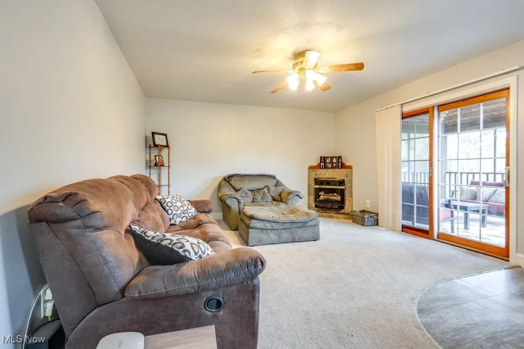 Carpeted living room with ceiling fan and a fireplace with raised hearth