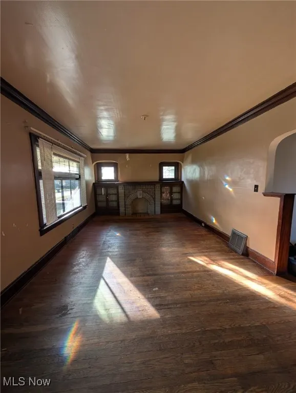 Spare room with ornamental molding, dark wood-type flooring, a fireplace, and arched walkways