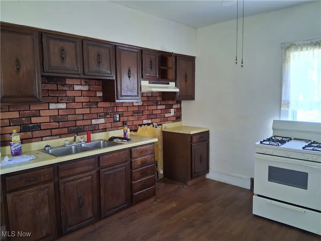 Kitchen with white range with gas stovetop, light countertops, dark brown cabinets, dark wood-style flooring, and decorative backsplash