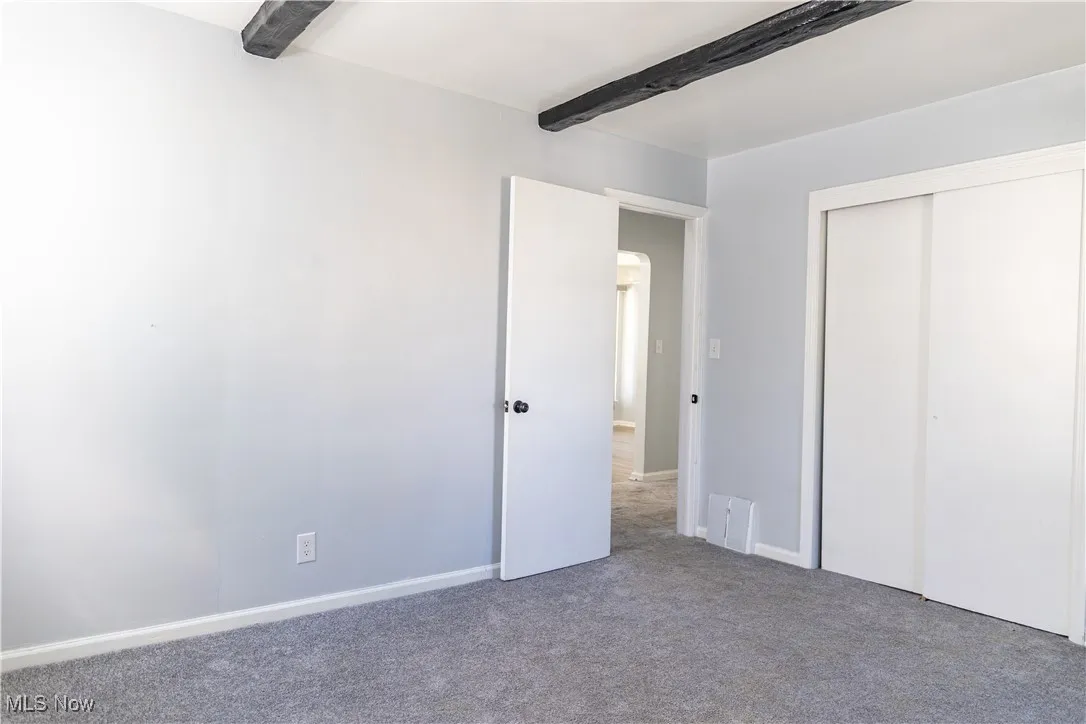Bedroom featuring carpet flooring, beam ceiling, and a closet