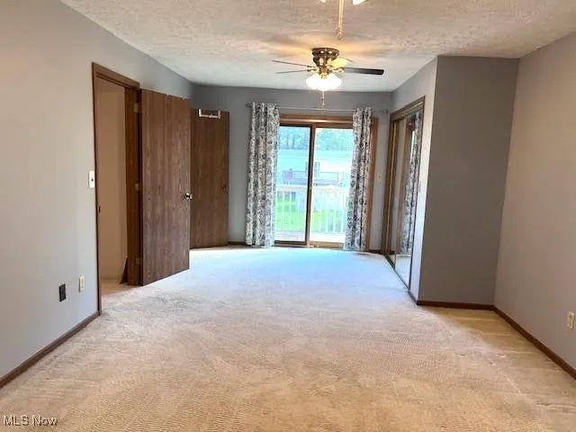Master bedroom, with slider doors to balcony, textured ceiling, and ceiling fan. Double closet doors are mirrored and full bath is opposite the slider on the left. Cream colored carpet, freshly cleaned.