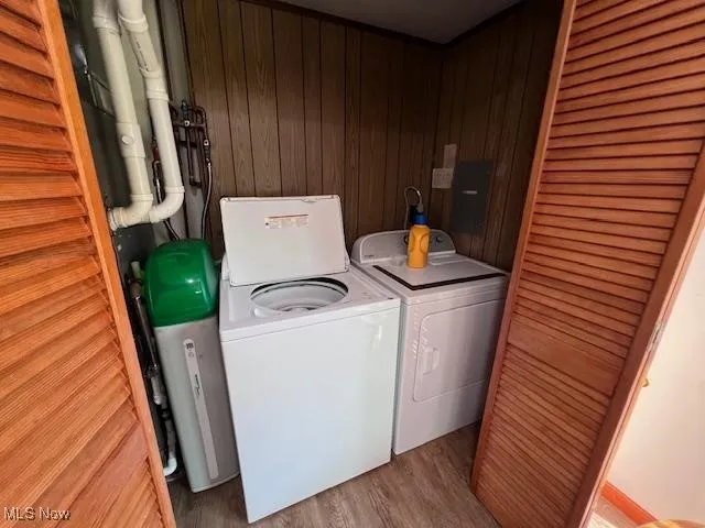 Laundry area with paneled walls, washer and clothes dryer, light wood-type flooring, hidden behind bi-fold doors.