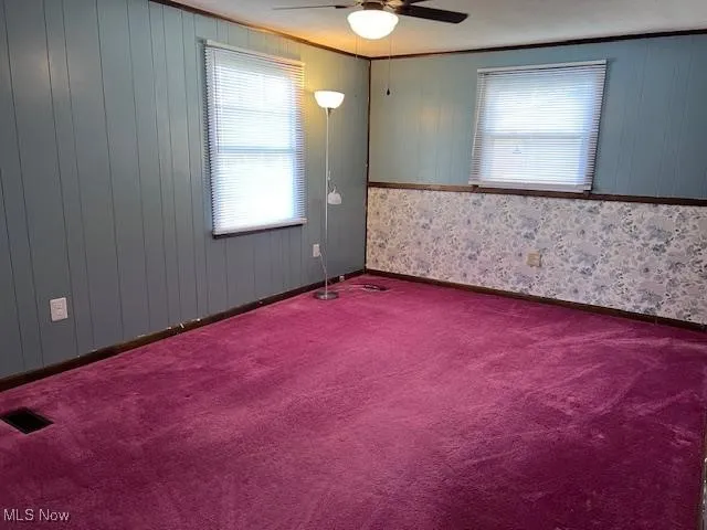 Nice size room featuring dark colored carpet, wooden walls, and ceiling fan