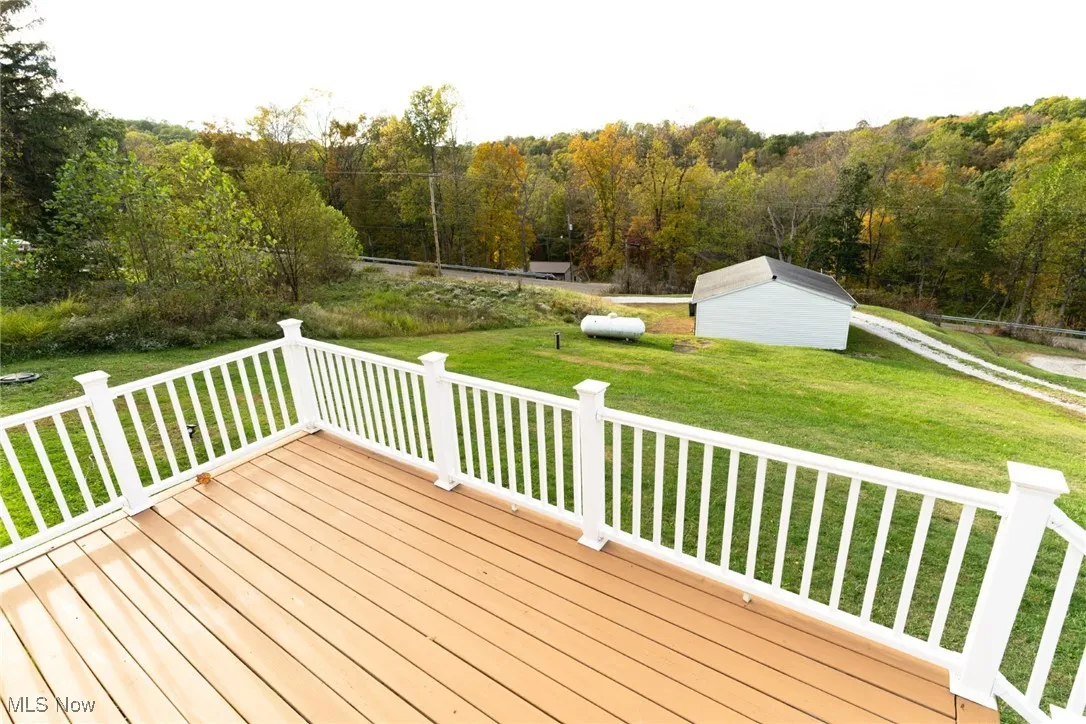 Wooden terrace featuring a forest view, a lawn, and an outbuilding