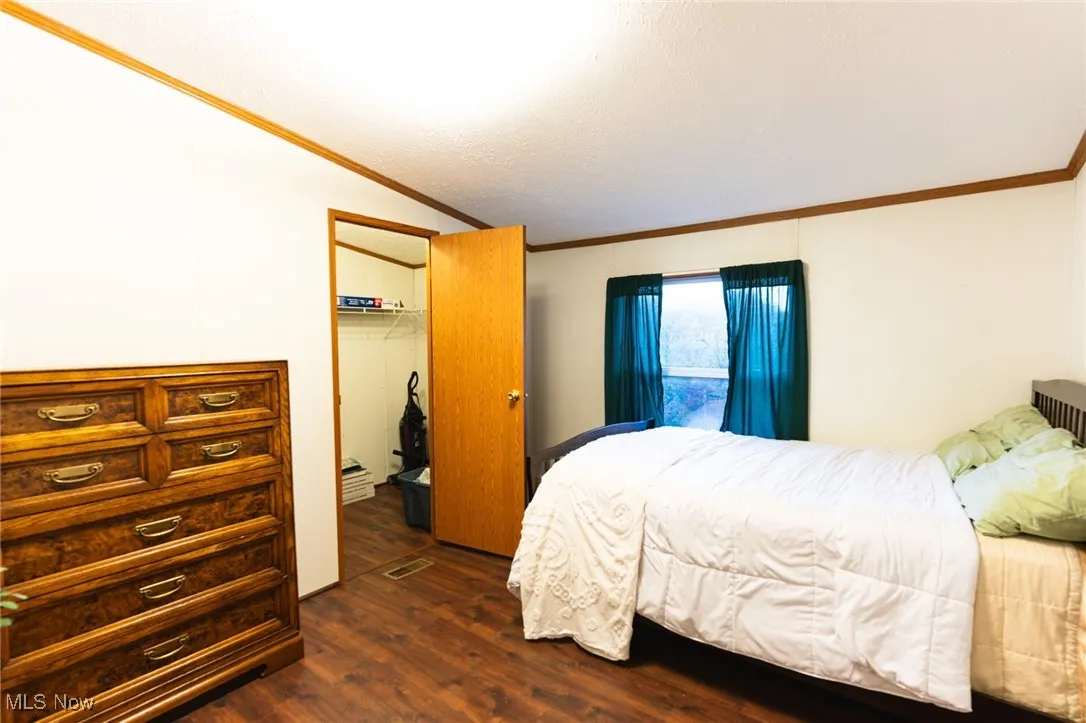 Bedroom featuring dark wood-style flooring, crown molding, a closet, and vaulted ceiling