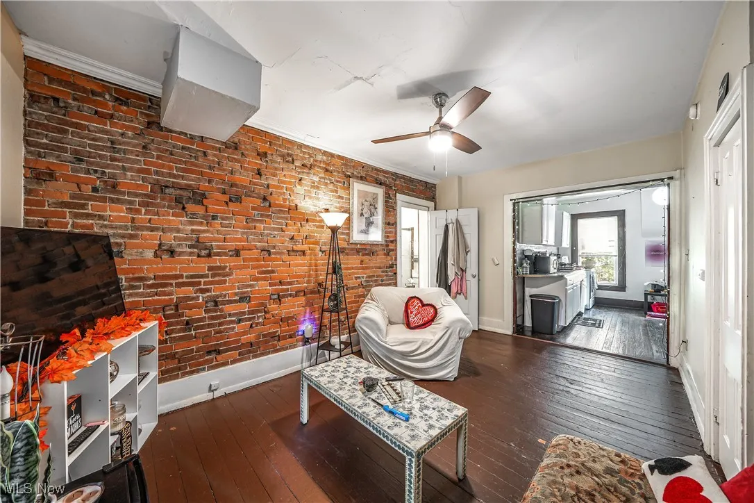 Sitting room featuring brick wall, dark wood-type flooring, a ceiling fan, and ornamental molding