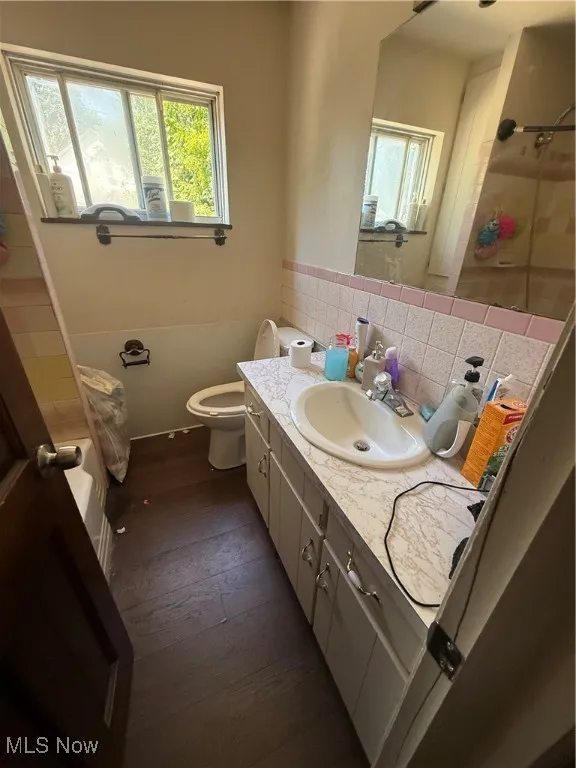 Bathroom with vanity, dark wood-type flooring, tile walls, and tiled shower / bath