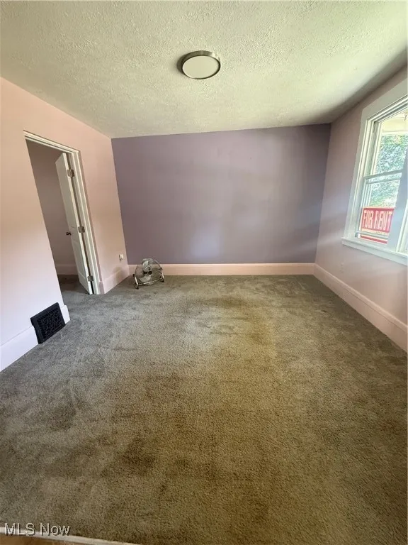 Empty room with a textured ceiling and carpet floors