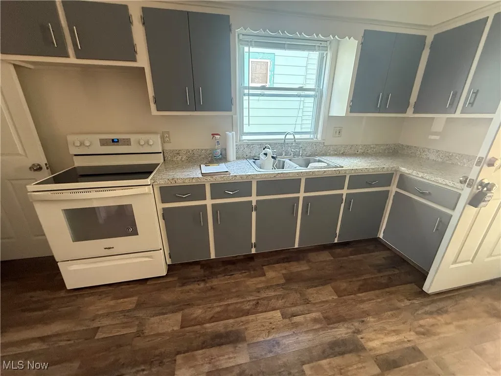 Kitchen with white range with electric stovetop, light countertops, and dark wood-type flooring