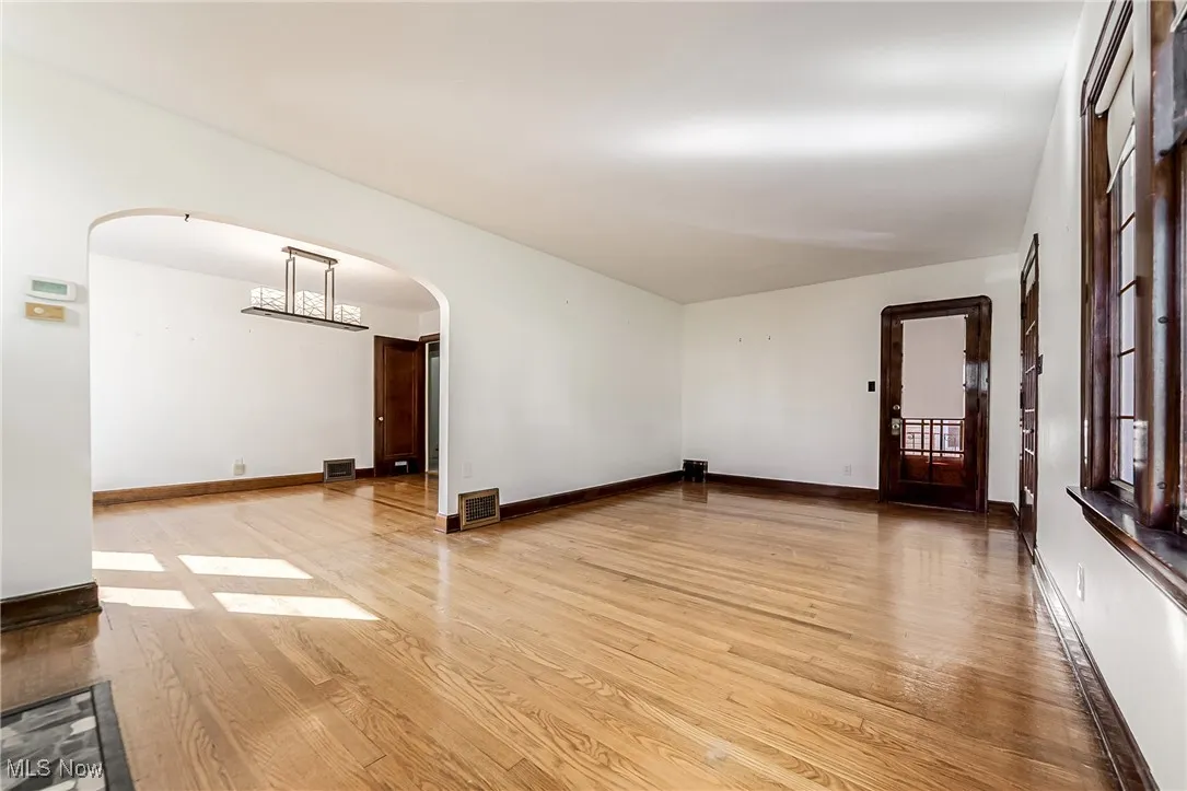 Unfurnished room with light wood-style floors, arched walkways, and a chandelier
