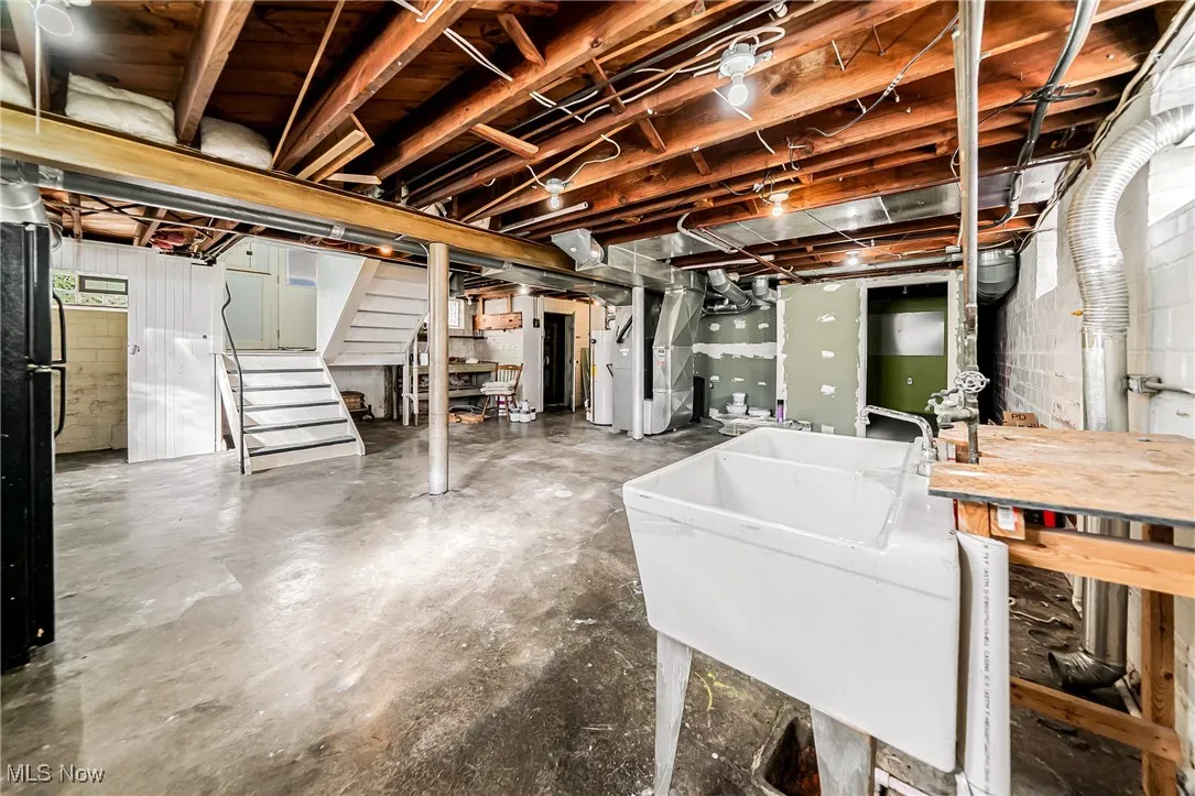 Unfinished below grade area with stairs, freestanding refrigerator, heating unit, and gas water heater