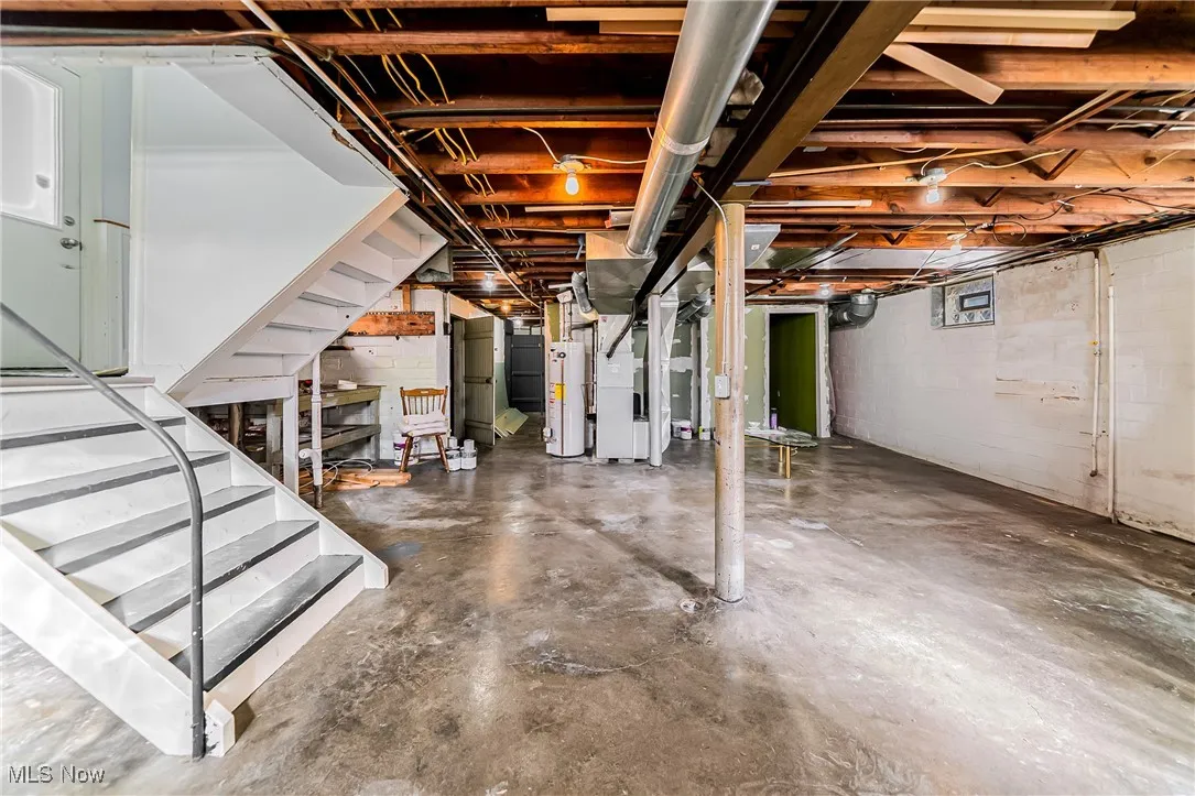 Unfinished basement featuring stairs, water heater, and heating unit