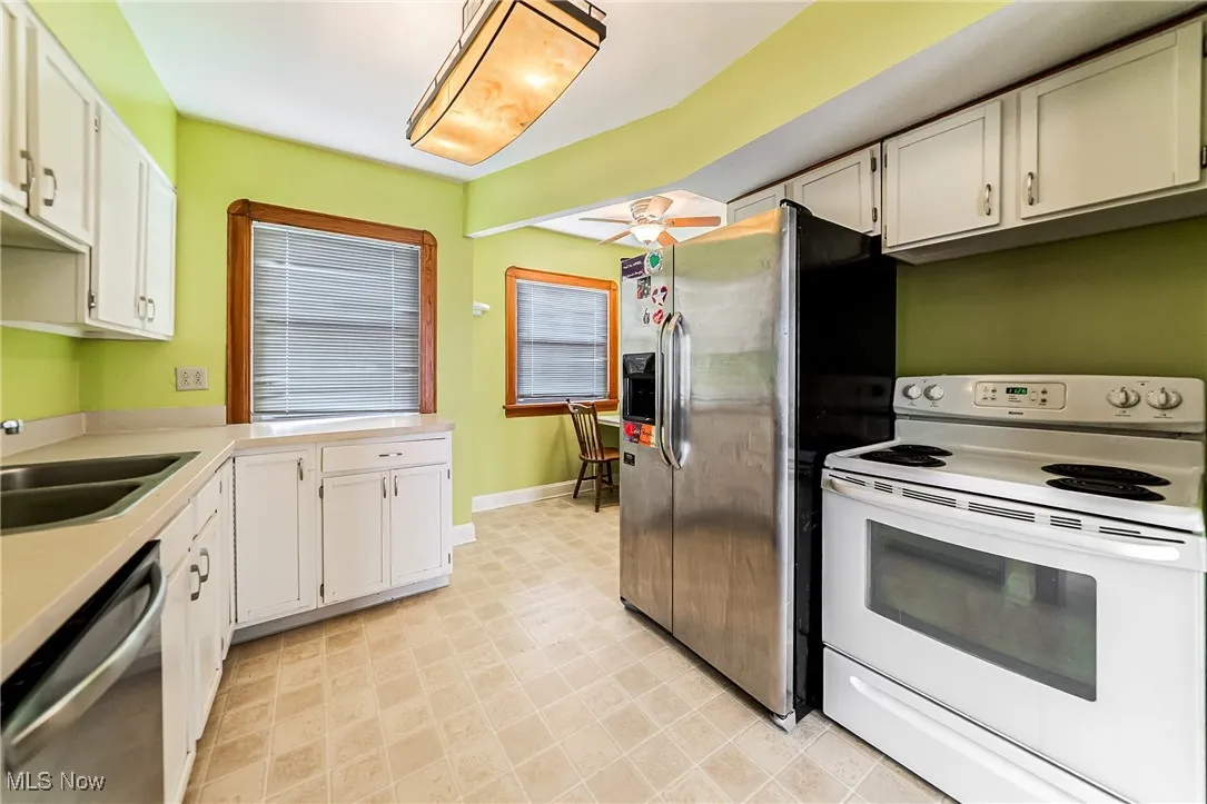 Kitchen with stainless steel appliances, white cabinets, light countertops, and ceiling fan