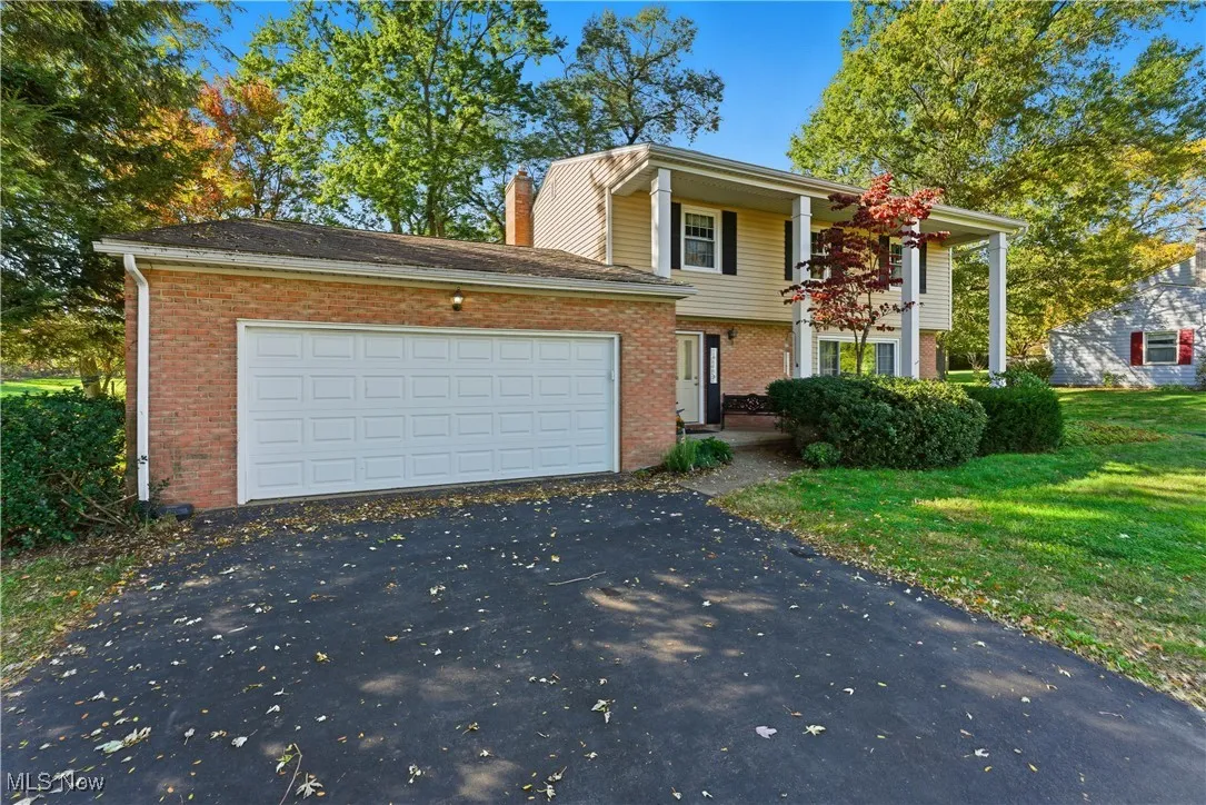View of front of property featuring brick siding, driveway, an attached garage, and a chimney
