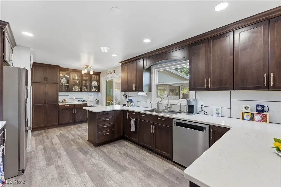 Kitchen featuring glass insert cabinets, a peninsula, stainless steel appliances, light wood finished floors, and dark brown cabinetry