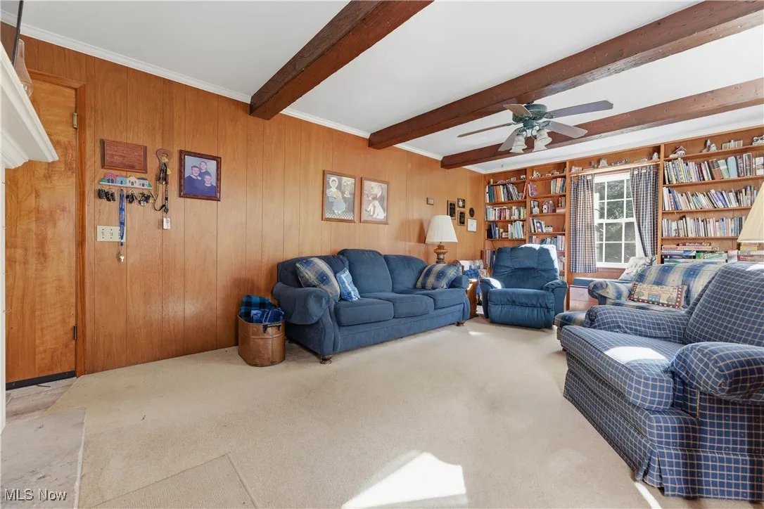 Carpeted living room featuring wood walls and beamed ceiling