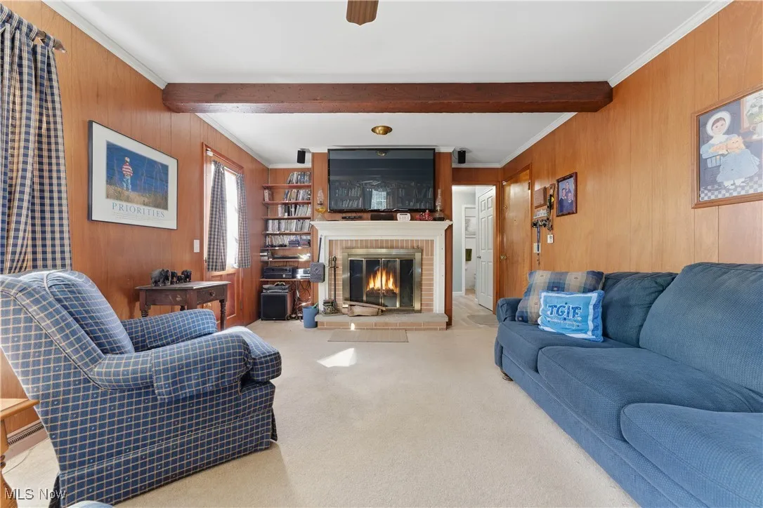 Living area featuring wooden walls, beamed ceiling, a fireplace, ornamental molding, and carpet floors