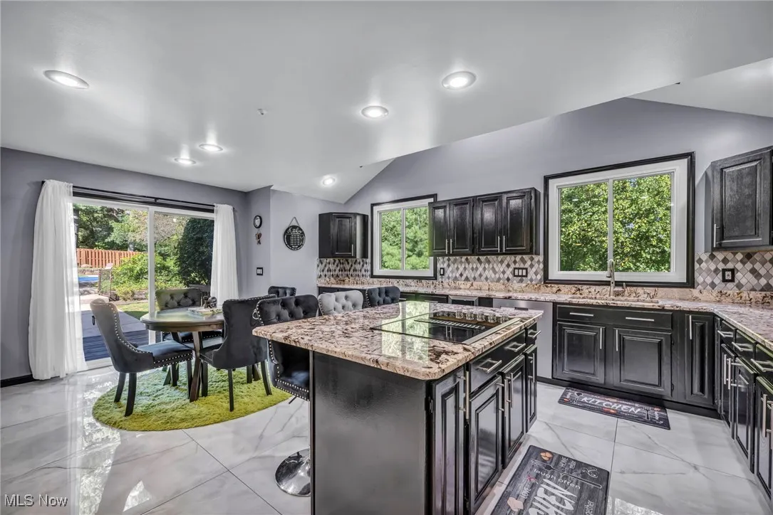 Kitchen with decorative backsplash, light stone countertops, a center island, dark cabinetry, and light marble finish floors