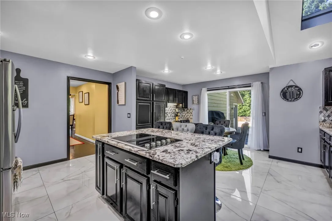 Kitchen featuring dark cabinets, a center island, light marble finish floors, freestanding refrigerator, and light stone counters