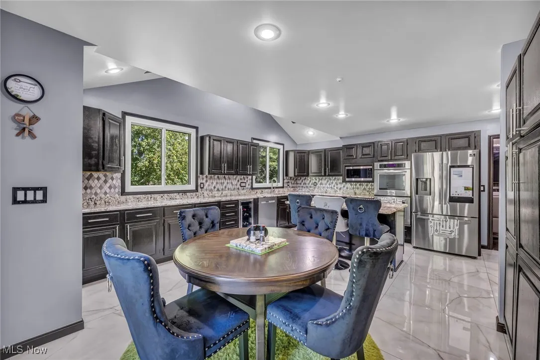 Dining room with lofted ceiling, light marble finish flooring, wine cooler, and recessed lighting