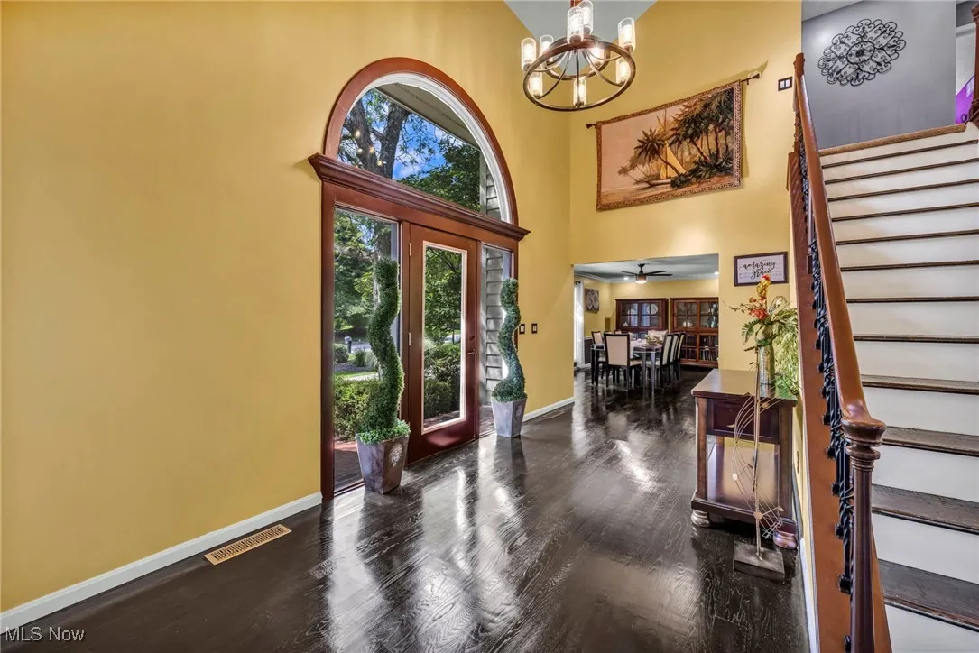 Foyer entrance with stairway, a towering ceiling, dark wood finished floors, a chandelier, and a ceiling fan