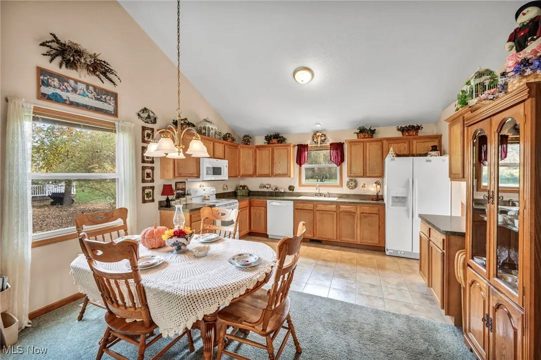 Dining area with vaulted ceiling, light tile patterned flooring, light carpet, and a chandelier