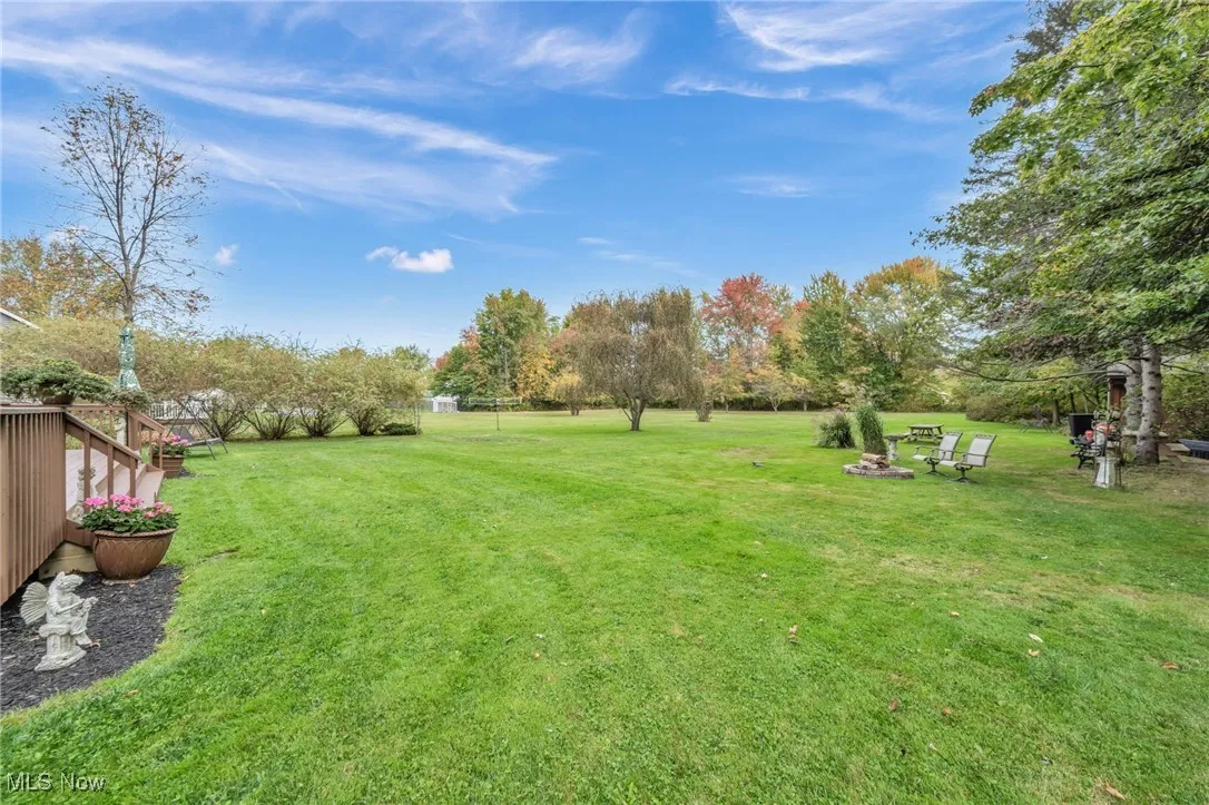 View of grassy yard featuring a wooden deck and view of scattered trees