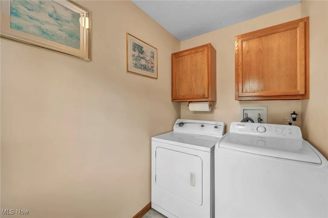 Laundry area featuring a textured ceiling, washer and dryer, and cabinet space