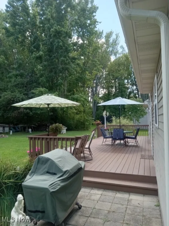 Wooden deck featuring outdoor dining area, area for grilling, a yard, and view of wooded area