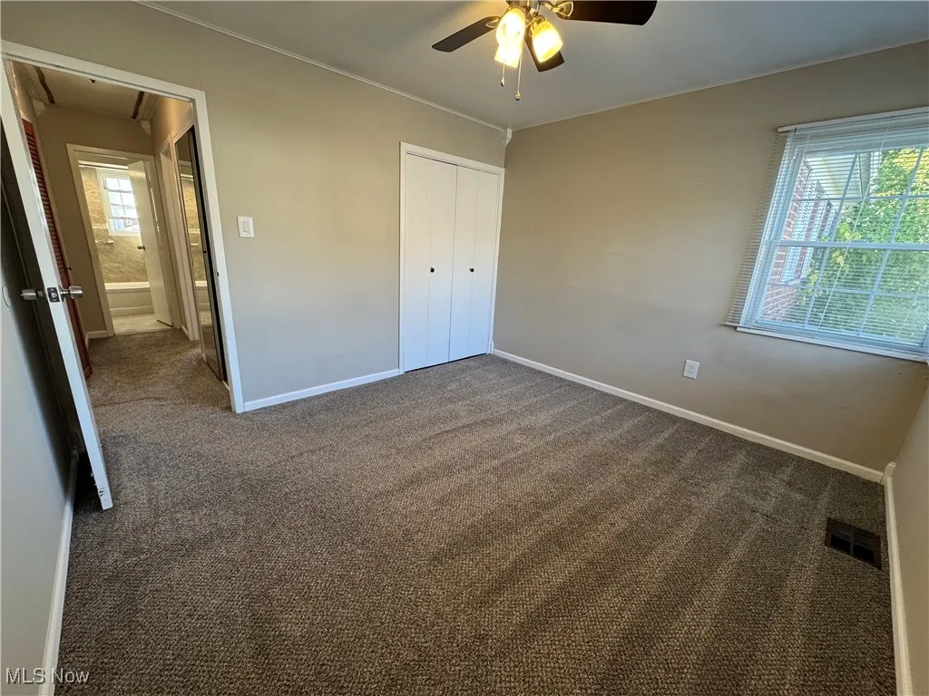 Unfurnished bedroom with dark colored carpet, a closet, attic access, and ceiling fan