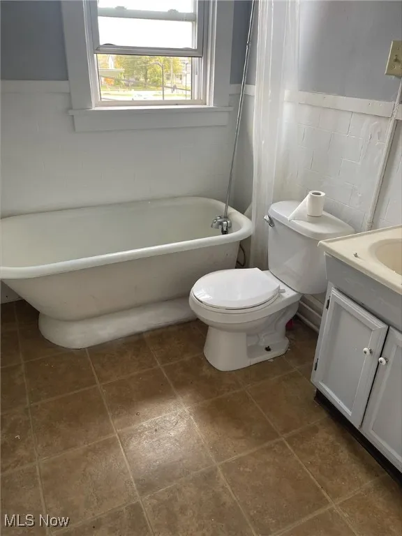 Bathroom with a soaking tub, vanity, a wainscoted wall, and tile walls