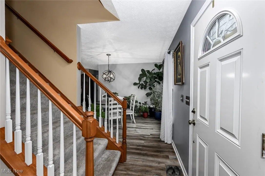 Foyer entrance featuring a textured ceiling, dark wood-style floors, a chandelier, and stairs
