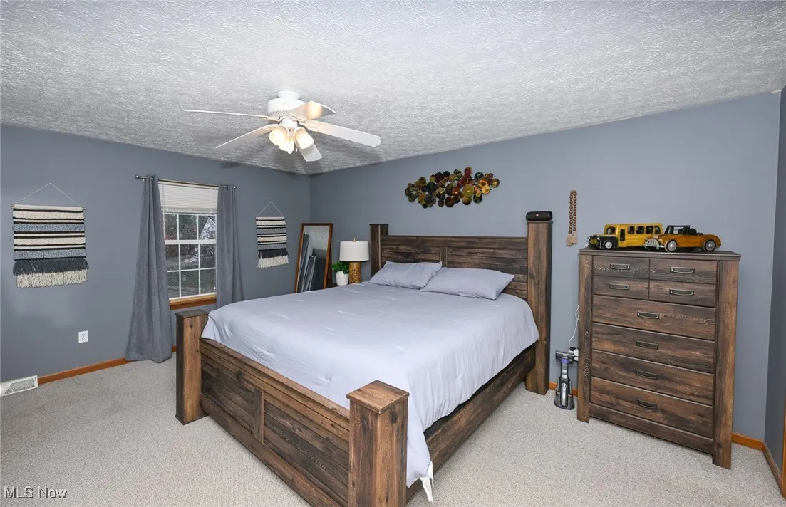 Carpeted bedroom featuring ceiling fan and a textured ceiling