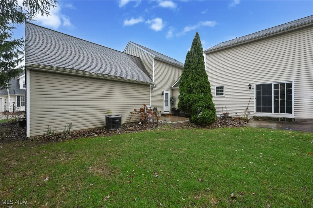 Rear view of property with roof with shingles, a lawn, and a patio area