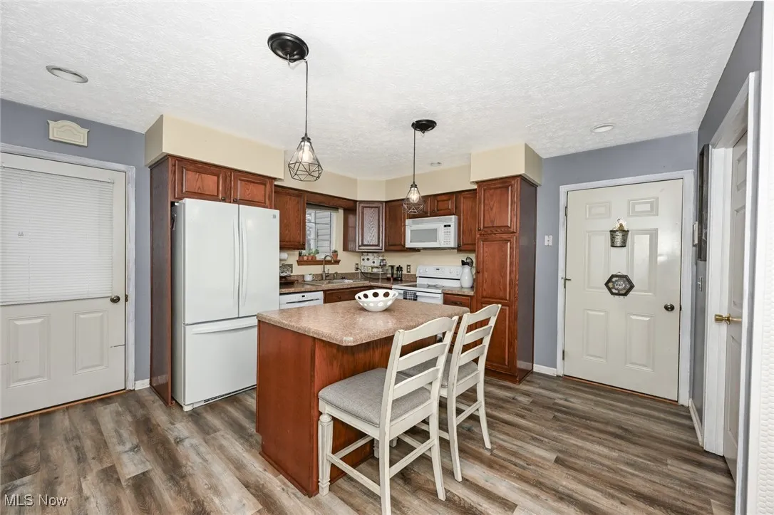 Kitchen featuring a center island, white appliances, a breakfast bar, pendant lighting, and a textured ceiling