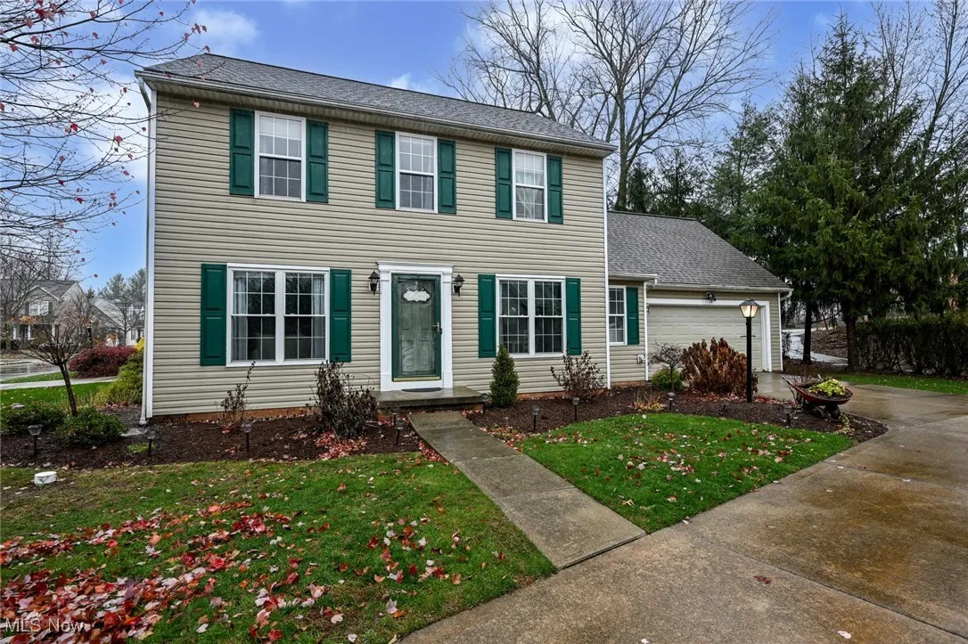 Colonial house with a front lawn, roof with shingles, an attached garage, and driveway