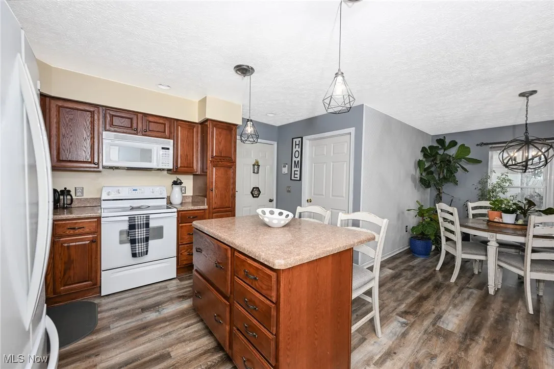 Kitchen featuring white appliances, pendant lighting, light countertops, dark wood-style floors, and a kitchen island