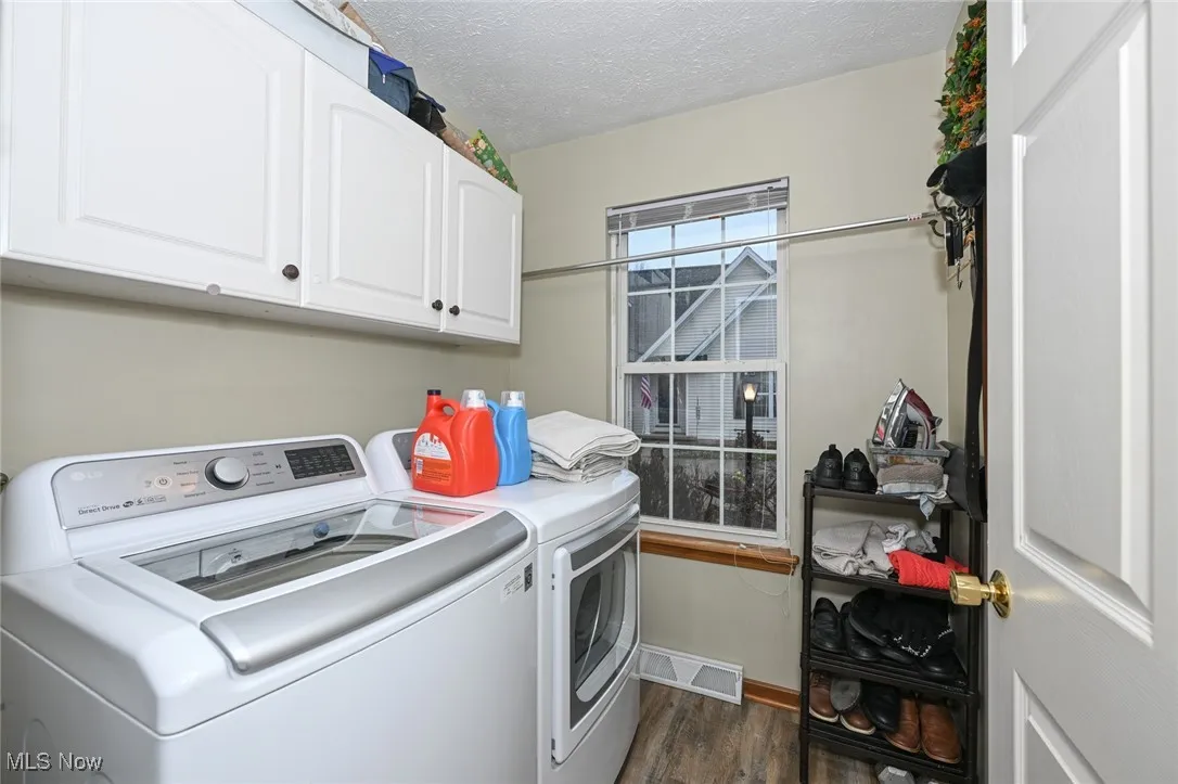 Main Level - Washroom featuring dark wood-type flooring, a textured ceiling, cabinet space, and washer and dryer
