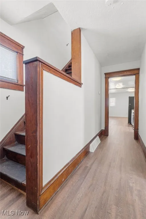 Corridor with stairs, wood finished floors, and a textured ceiling